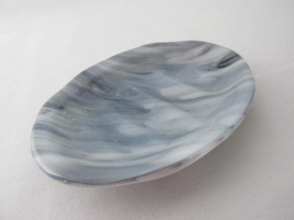 A flat, oval-shaped soap dish featuring a black on white streaky design, resting on a white surface.