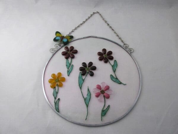 Circular stained glass panel named GA14004, featuring vibrant flowers and a butterfly at the top, suspended by a chain for hanging as garden or wall art.