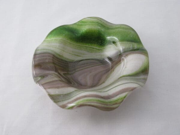 A bowl that is made of glass and has green, brown and white swirls.