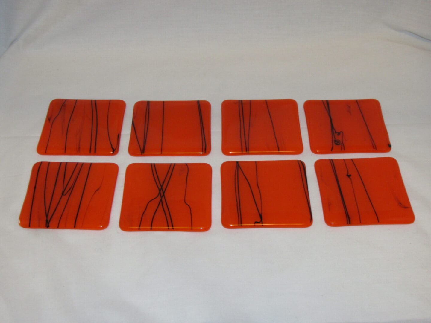 A set of eight orange coasters with black lines.