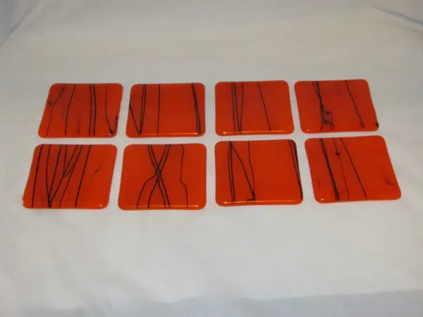 A set of eight orange coasters with black lines.