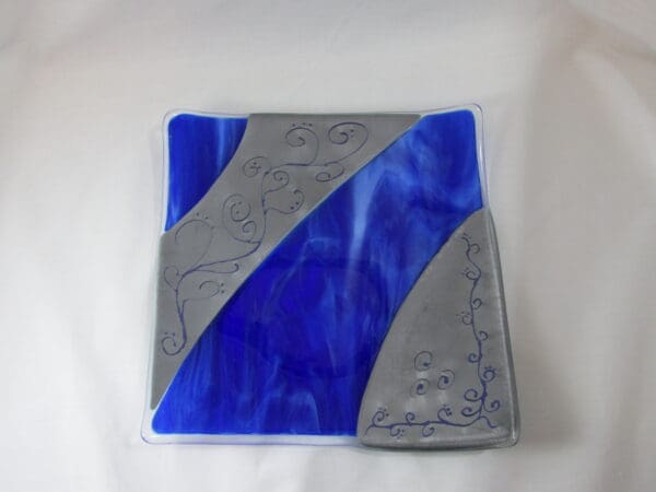 A blue and gray glass coaster with a design on it.