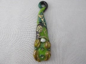 A green and yellow glass bead is hanging on a white cloth.