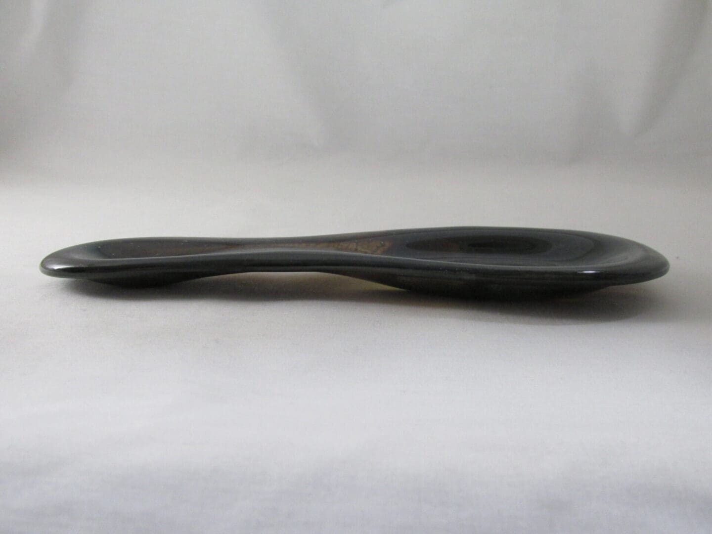 Twisted black ceramic spoon on white background.